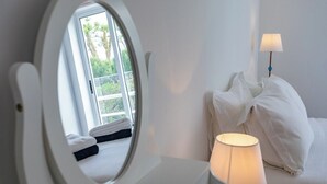 Hotellihuone, jossa on sänky, yöpöytälamppu, ikkuna, josta on näkymä vehreään maisemaan, ja peili.