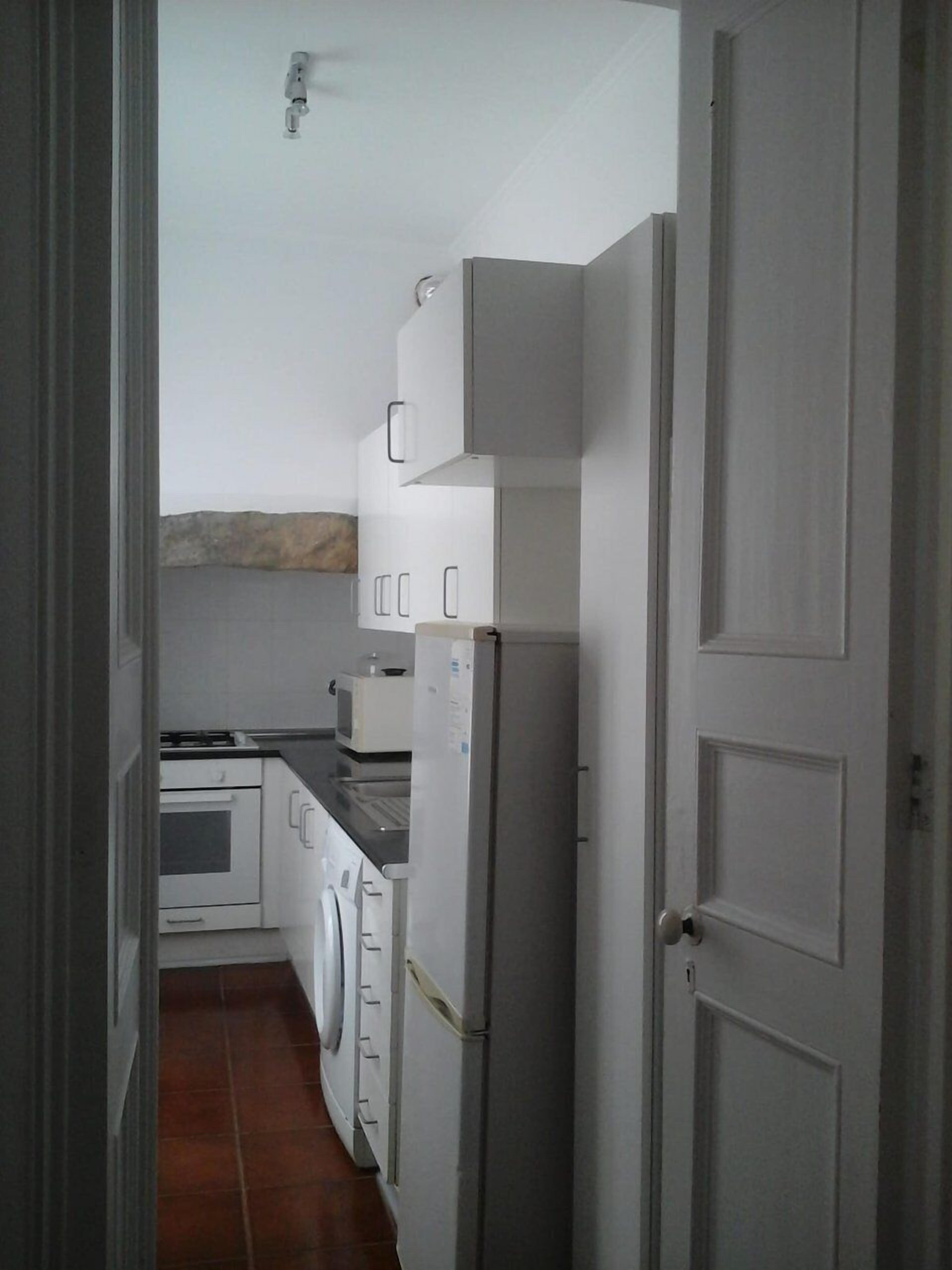 A narrow kitchen with white cabinets, a refrigerator, a microwave, and a stove.
