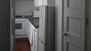 A narrow kitchen with white cabinets, a refrigerator, a microwave, and a stove.