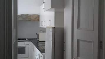 A narrow kitchen with white cabinets, a refrigerator, a microwave, and a stove.