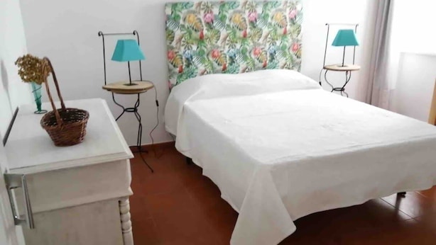 A bedroom with a bed, a small table with a lamp, and a decorative basket. - GuestReady - Cheerful Ponta Delgada townhouse (Ponta Delgada)