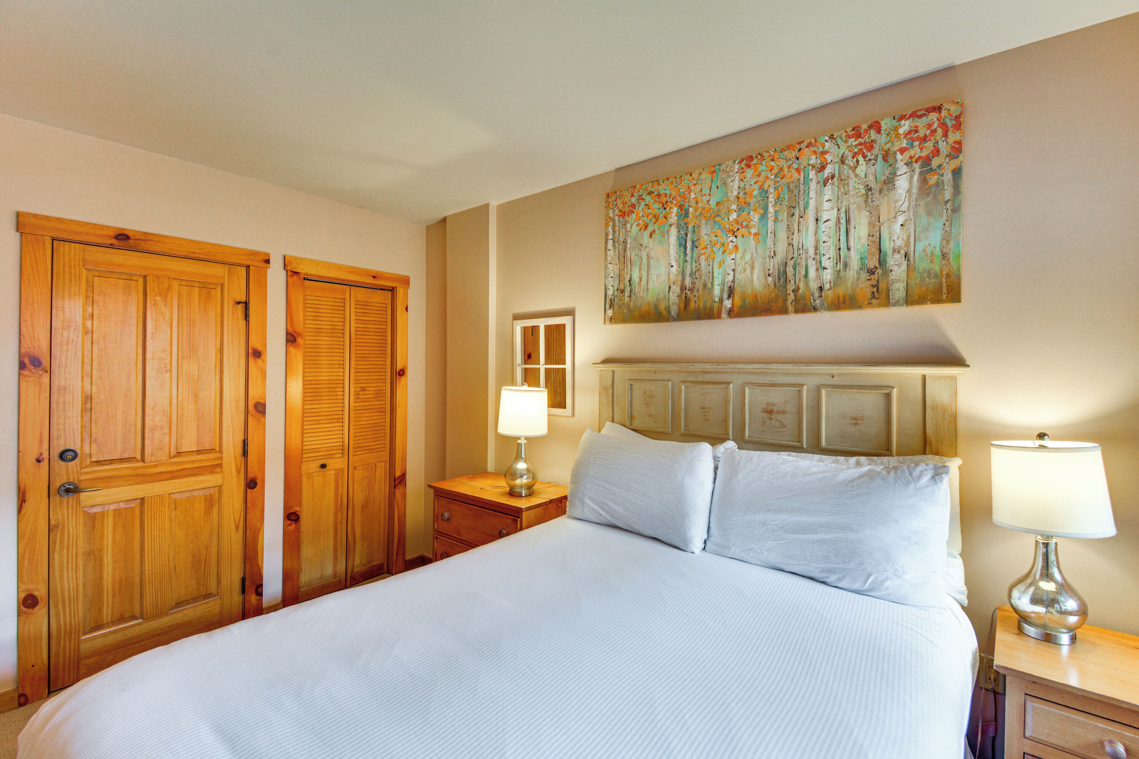 A hotel room with a large bed, wooden wardrobe, and a painting on the wall.