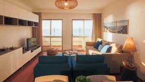 A modern living room with a sofa set, a TV, and a dining table. There is a large window with a view of the city. - GuestReady - Stunning TopFloor OceanView (Ponta Delgada)