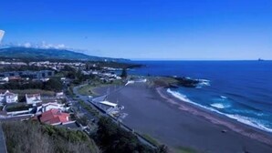 A coastal area with a beach, a road, and buildings in the background. - GuestReady - Stunning TopFloor OceanView (Ponta Delgada)