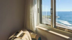 A room with a large window overlooking the sea, a bed, and a bedside table with a book and a remote control. - GuestReady - Stunning TopFloor OceanView (Ponta Delgada)