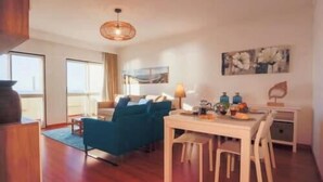 A modern living room with a blue sofa, a dining table, and a hanging light fixture. - GuestReady - Stunning TopFloor OceanView (Ponta Delgada)