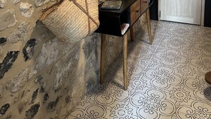 A room with a stone wall, a wooden door, a black console table with woven baskets, and a patterned floor. - The Touline Apple **** (Fécamp)
