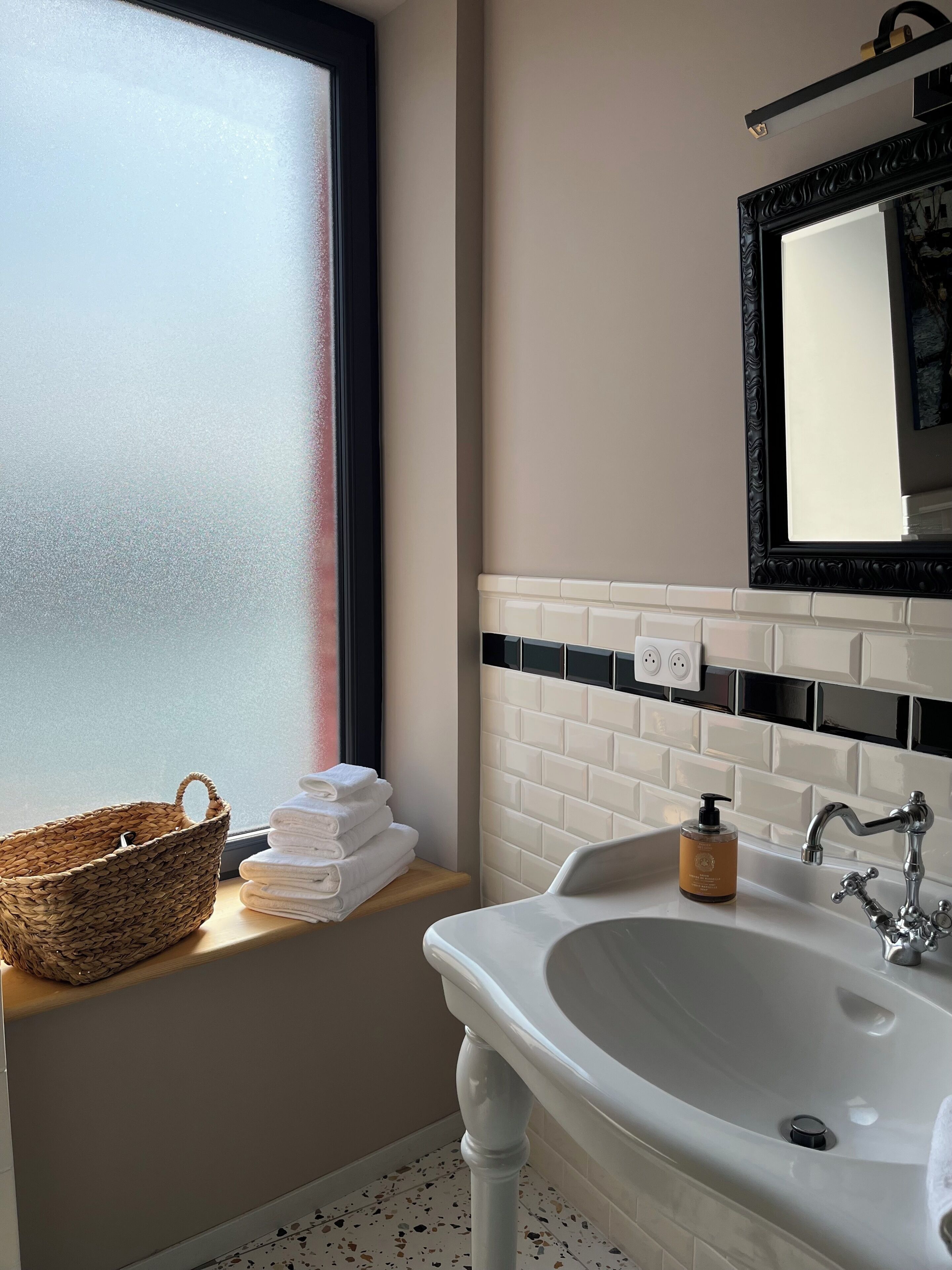 Une salle de bain avec un lavabo blanc, un miroir, une fenêtre et un panier rempli de serviettes.