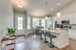 A modern kitchen with white cabinetry, a central island with bar stools, and a dining area with a table and chairs. - Modern Family Home w/ Spacious Yard in Milton (Milton)
