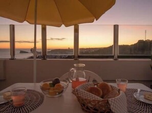 A table set for breakfast with a view of the sunset over the sea. - GuestReady - OceanView TopFloor w Terrace (Ponta Delgada)