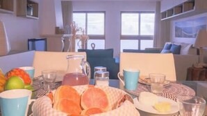 A dining area with a table set for breakfast, including fruits, bread, and beverages.