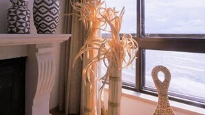 A room with a fireplace, a window with a view of the sea, and decorative vases on a shelf.