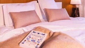 A hotel room with a bed, pillows, a bedside table with a lamp, and wall art above the bed.