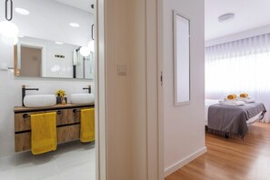 A modern bathroom with dual sinks, a large mirror, and yellow towels. - GuestReady - JB Comfort Flat (Ponta Delgada)