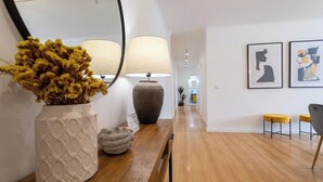 Un couloir doté d’un plancher en bois, d’un vase blanc contenant des fleurs séchées, d’une lampe et de deux œuvres d’art encadrées accrochées au mur.