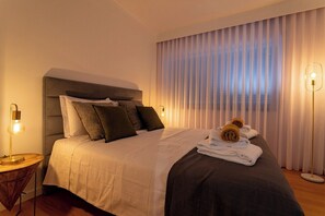 A hotel room with a bed, a nightstand, a lamp, and a window with curtains. - GuestReady - JB Comfort Flat (Ponta Delgada)
