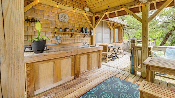 Um deck de madeira com área de bar, mesas ao ar livre e vista para árvores.