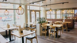Un café moderno con mesas y sillas de madera, amplios ventanales y lámparas colgantes.