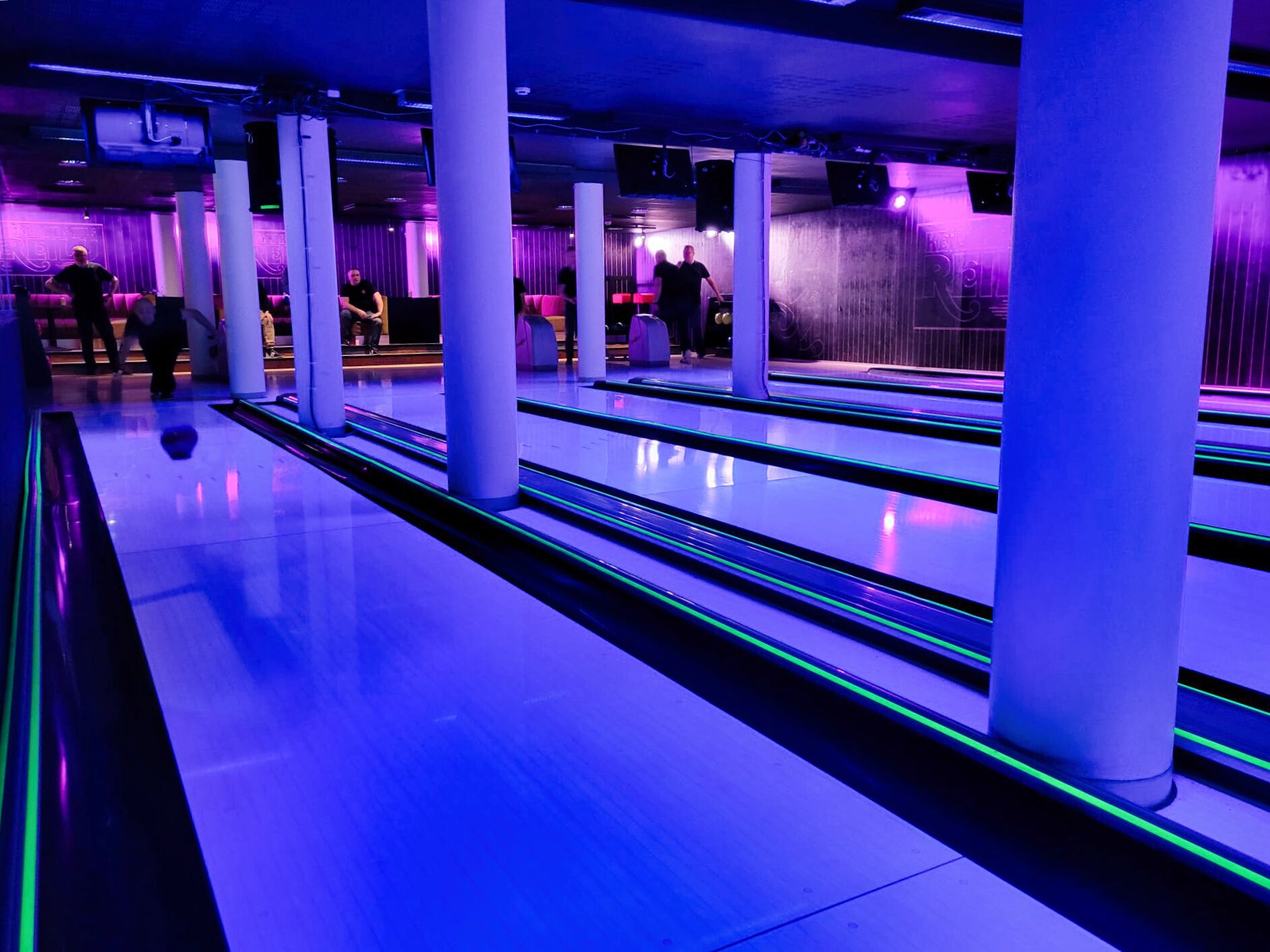 A bowling alley with multiple lanes, white columns, and purple lighting.