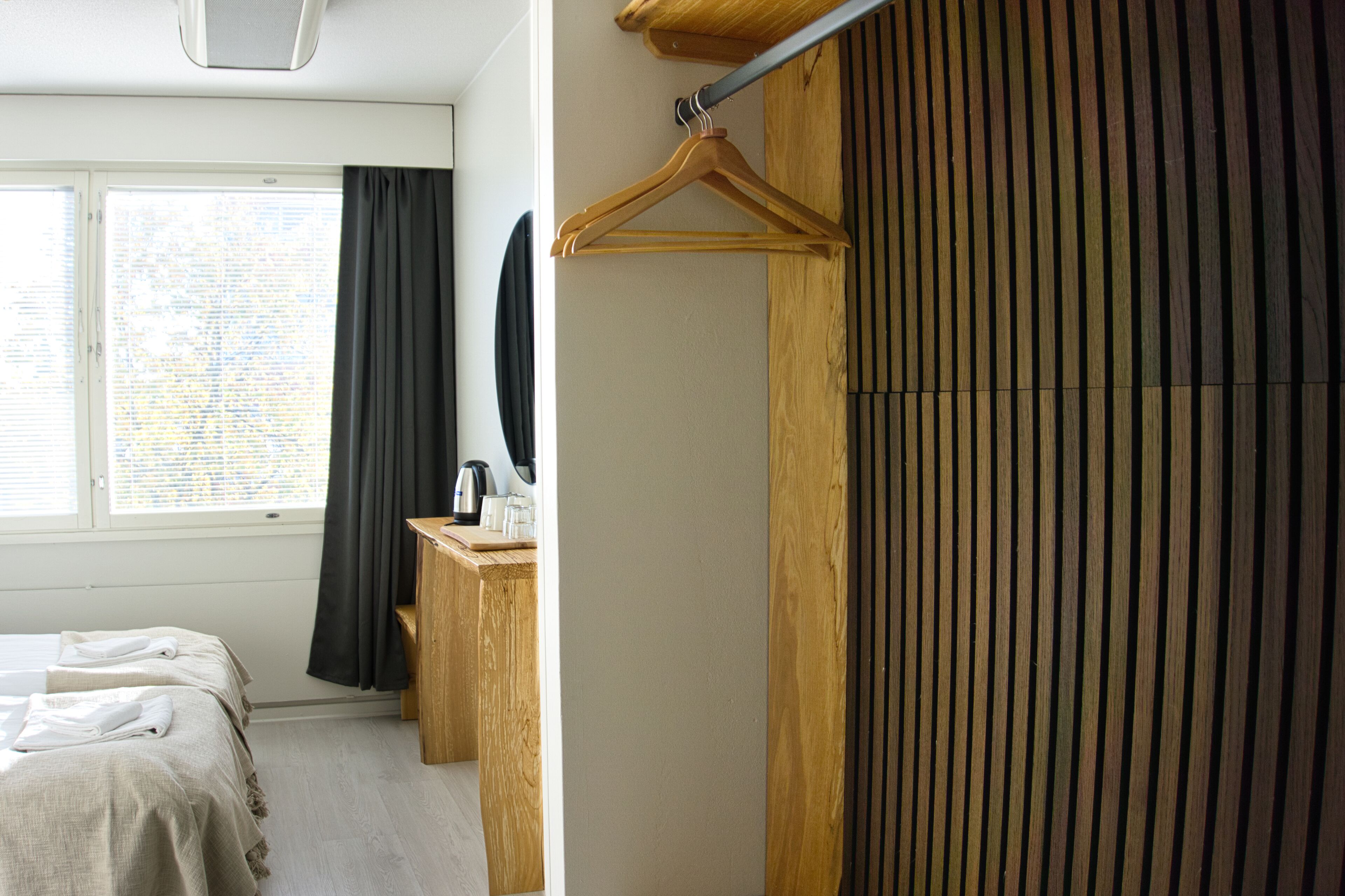 A hotel room with a bed, a wooden dresser, a mirror, and a window with curtains.