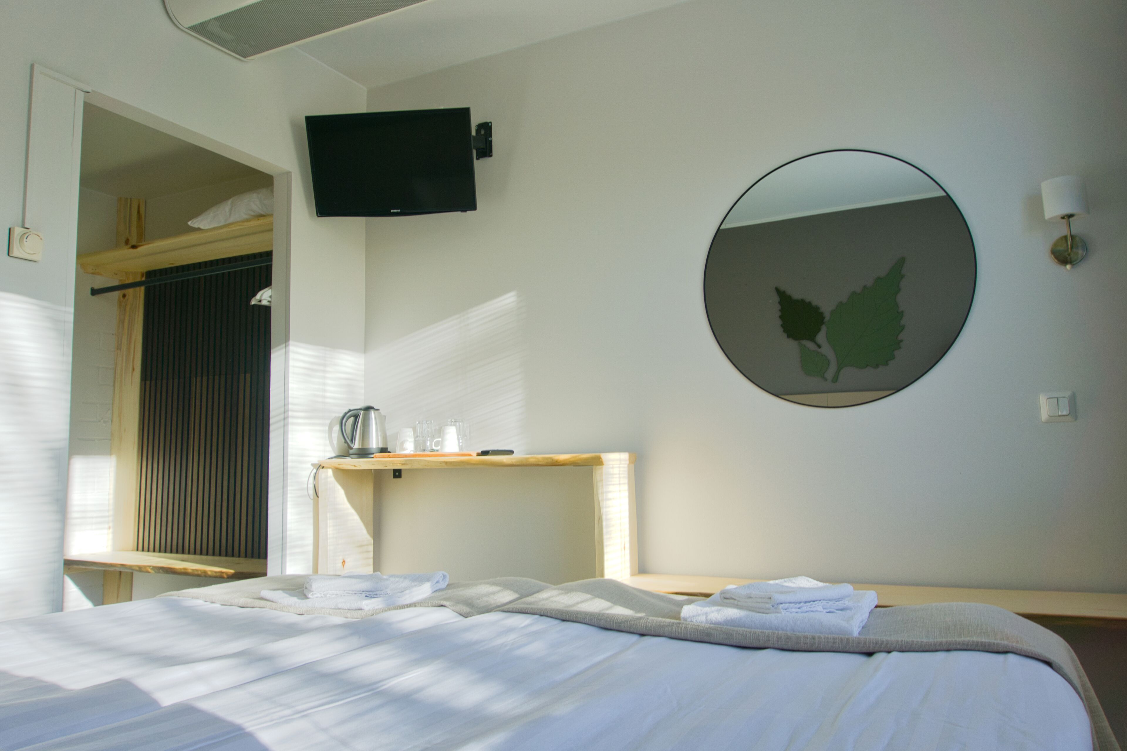 Ein Hotelzimmer mit einem Bett, einem an der Wand befestigten Fernseher, einem Spiegel und einem kleinen Tisch mit Wasserkocher und Gläsern.