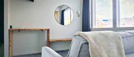 Ett modernt vardagsrum med en grå soffa, en rund spegel, en träbänk och en tv som är monterad på väggen.