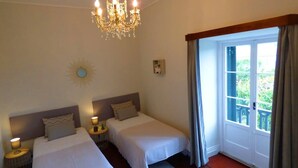 A hotel room with two beds, a chandelier, a sunburst mirror, and a view of greenery through a window. - GuestReady - Quinta do Solar perfect for families (Ponta Delgada)
