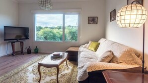 A living room with a sofa, a coffee table, a TV, and a large window with a view of greenery. - GuestReady - Quinta do Solar perfect for families (Ponta Delgada)