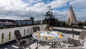 A round table with chairs and a table umbrella on a terrace with a view of houses and a church in the background. - GuestReady - Quinta do Solar perfect for families (Ponta Delgada)