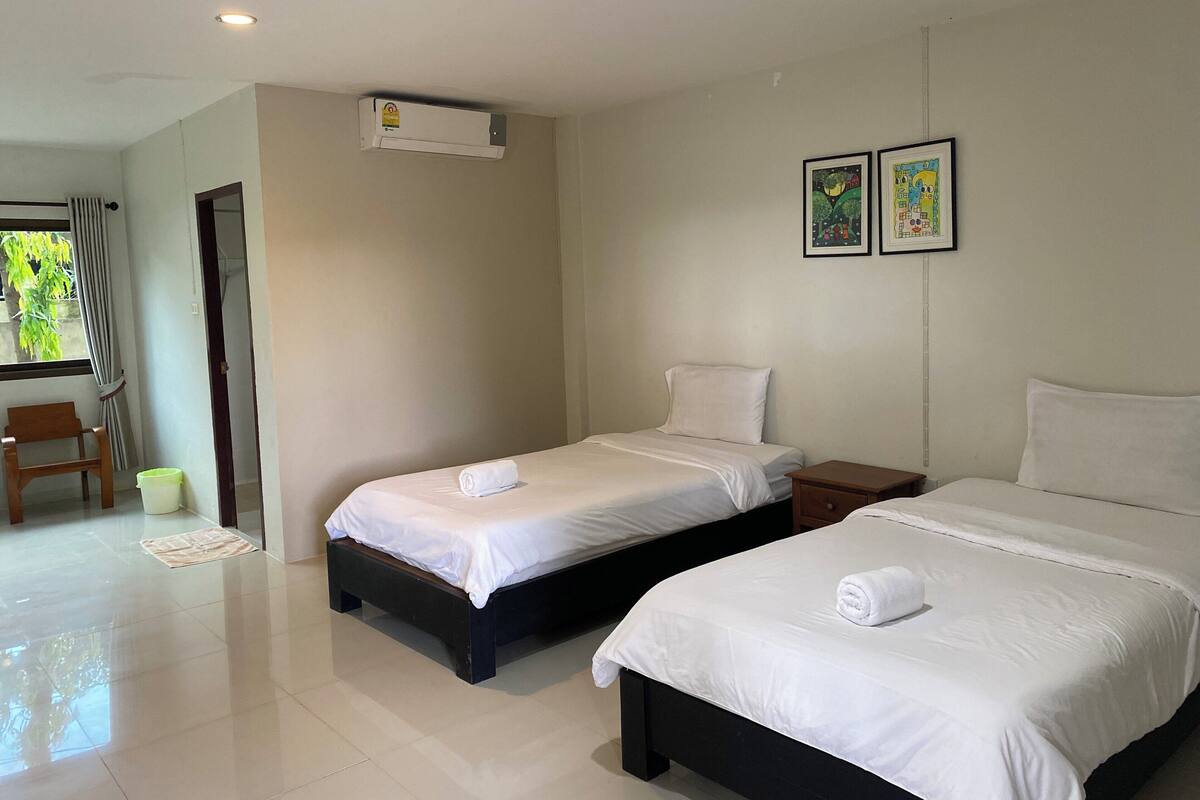 A hotel room with two beds, a window with curtains, a radiator, and a wall-mounted air conditioner.