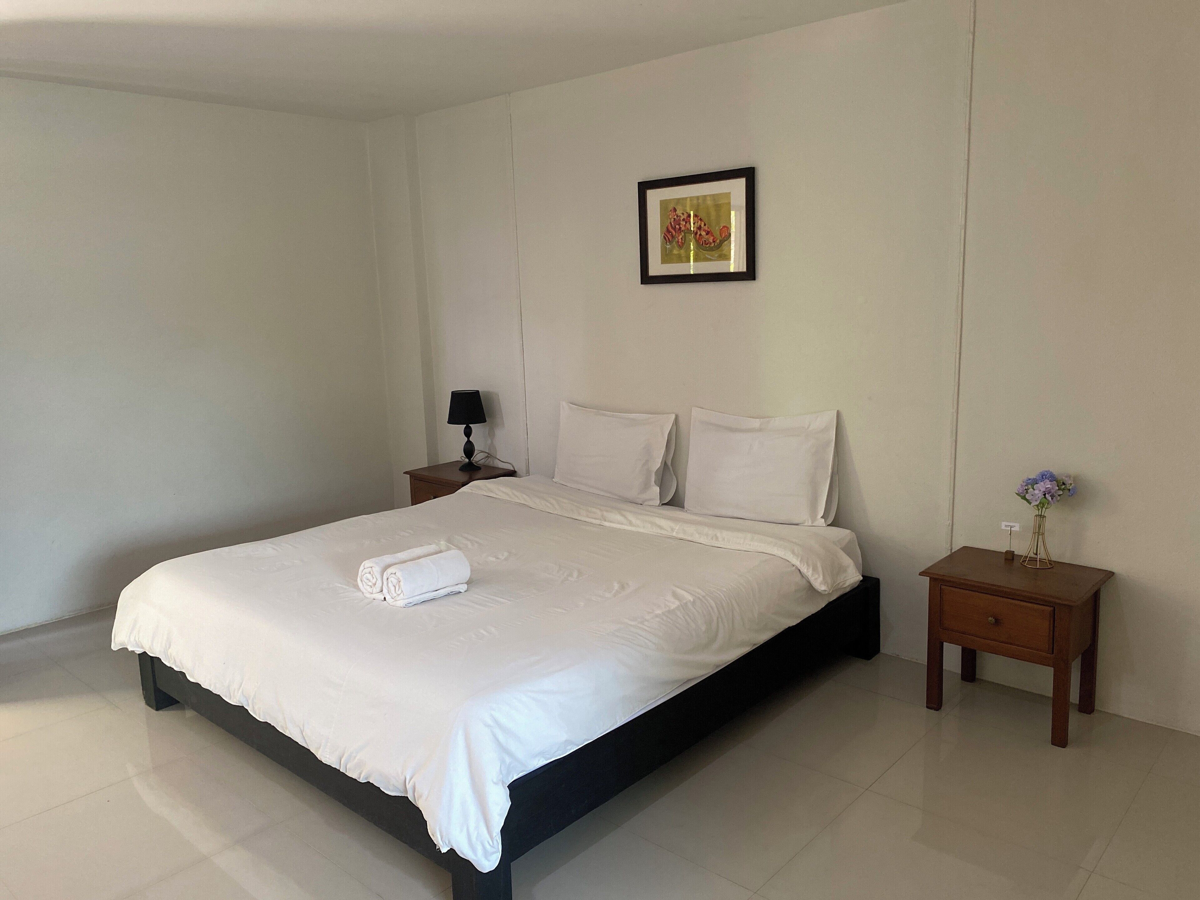 A neatly made bed with white linens, a small bedside table with a lamp, and a framed picture on the wall.