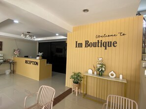 A reception area with a wooden wall displaying "Welcome to Im Boutique" and a reception desk. - IM BOUTIQUE HOTEL (Mae Sot)