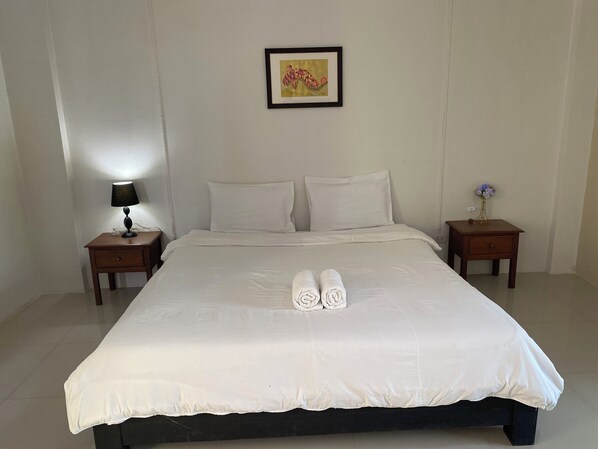 A neatly made bed with white linens, two pillows, and two rolled towels in the center. There is a framed picture on the wall above the bed. - IM BOUTIQUE HOTEL (Mae Sot)