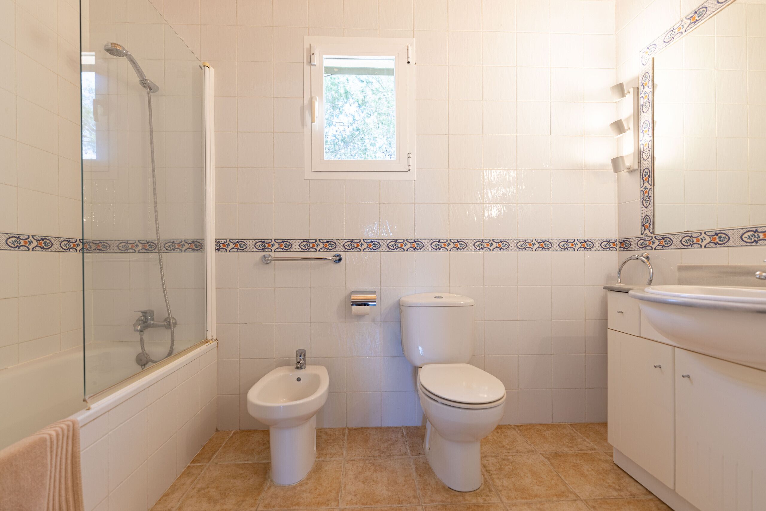 A bathroom with a shower, two toilets, a bidet, a window, and a sink.