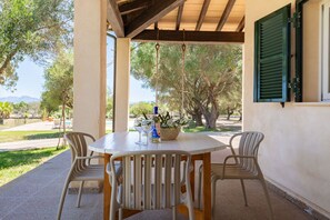 An outdoor patio with a round table, two chairs, a bottle of wine, and a basket of flowers.