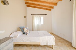 A bedroom with a bed, a wooden headboard, a window with curtains, and a tiled floor.
