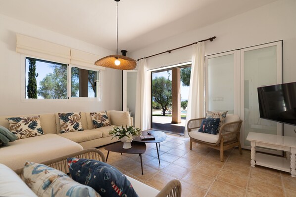 A spacious living room with a sofa, armchairs, a coffee table, and a television.