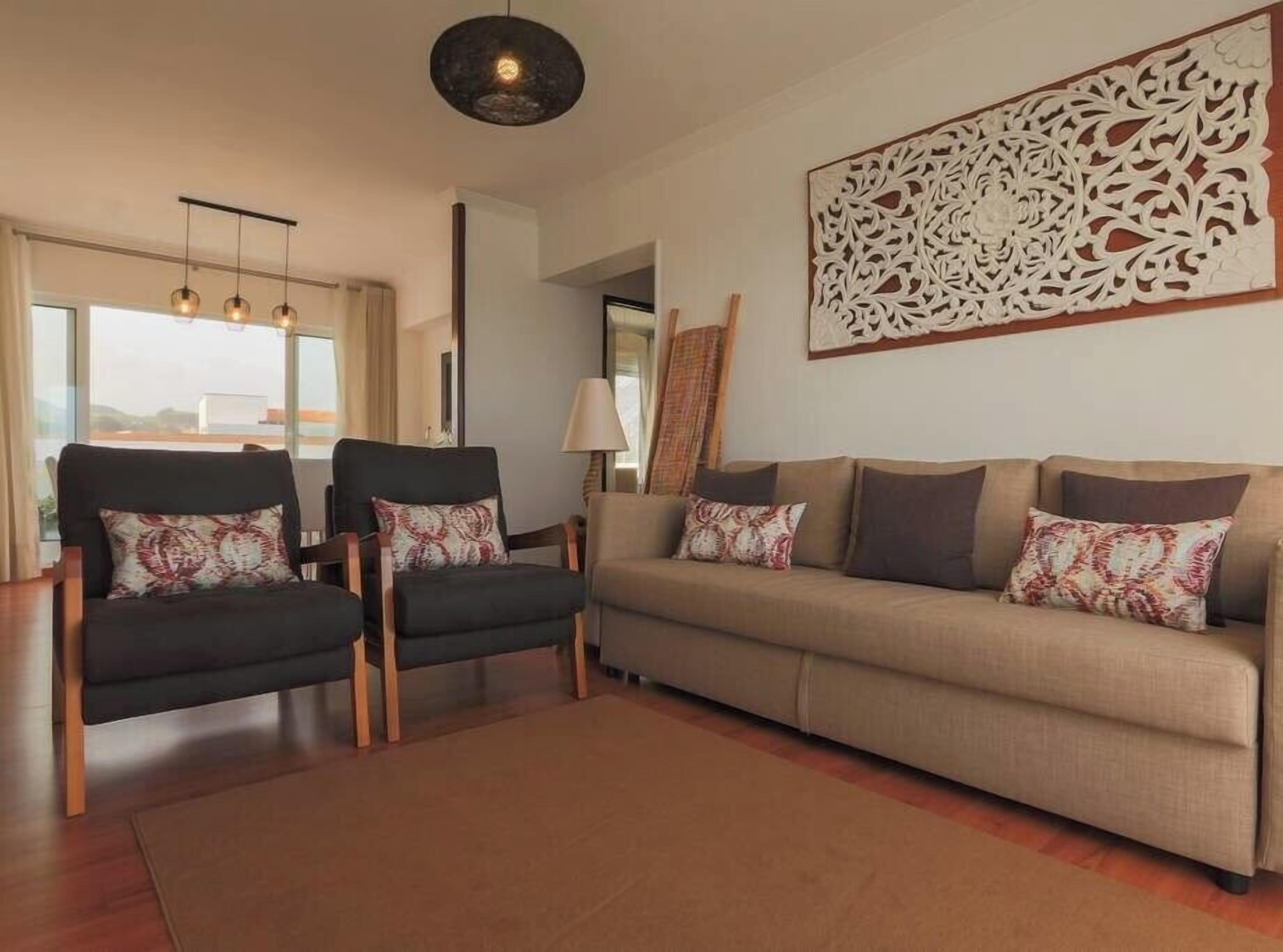 Un salon comprenant un canapé, deux fauteuils et un élément décoratif mural.