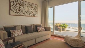 Uma sala de estar com sofá, uma poltrona e uma janela grande com vista para o mar.