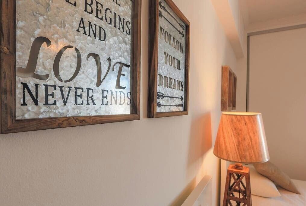 Two framed inspirational quotes on a wall, a wooden lamp, and a bed with pillows.