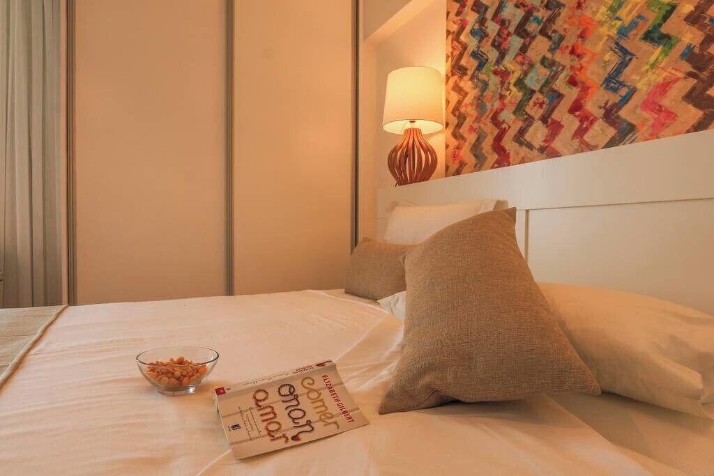 Una cama bien hecha con un libro y un cuenco de aperitivos, una pared con estampado, y una lámpara en una mesita de noche.