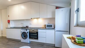 A compact kitchen with white cabinets, a washing machine, an oven, a microwave, and a refrigerator.