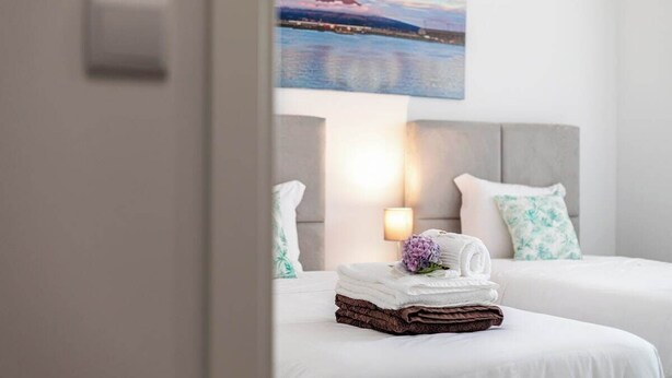 A hotel room with two beds, a painting of a mountain and water, and a nightstand with a lamp and towels.