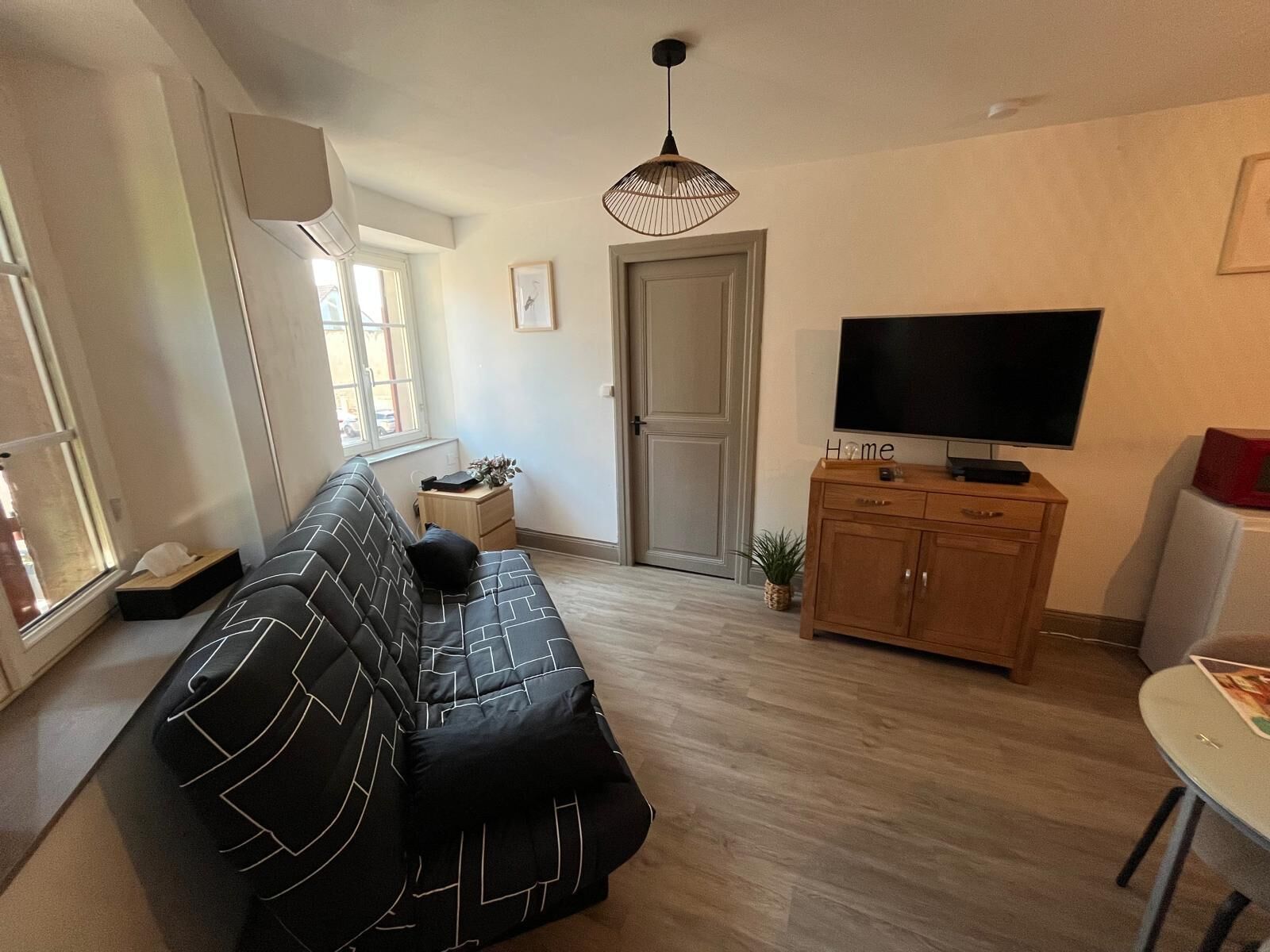 A modern living room with a black and white patterned sofa, a wooden cabinet, a television, and a small table.