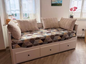 Un canapé blanc recouvert d’un tissu matelassé, avec deux coussins et une petite table d’appoint en bois.