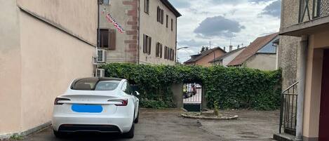 A narrow street with a white car parked on the left. There is a red arrow pointing forward on the ground.