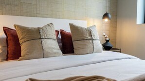 A neatly made bed with a white comforter and two pillows, a red pillow, and a black lamp on a bedside table.