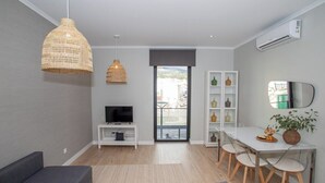 A modern living room with a sofa, TV, dining table, chairs, and a balcony with a view.