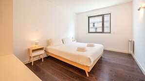 Une chambre à coucher avec un grand lit, une table de chevet avec une lampe, une fenêtre et un radiateur.