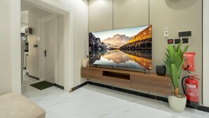 A modern living room with a large flat-screen TV on a wooden console, a fire extinguisher, and a potted plant.